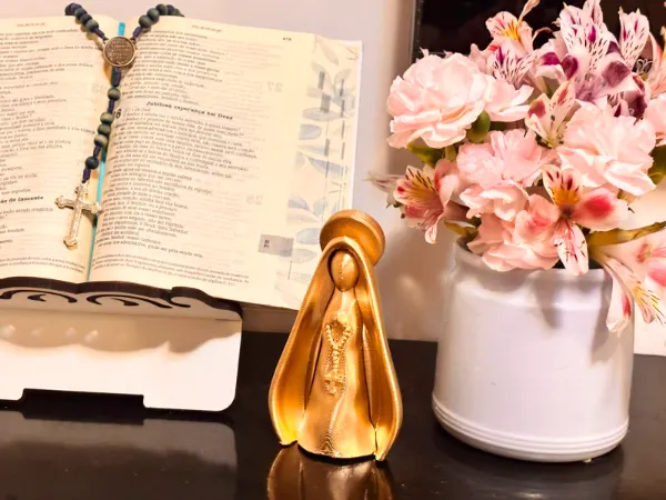 Imagem dourada de Nossa Senhora impressa em 3D ao lado de flores e bíblia